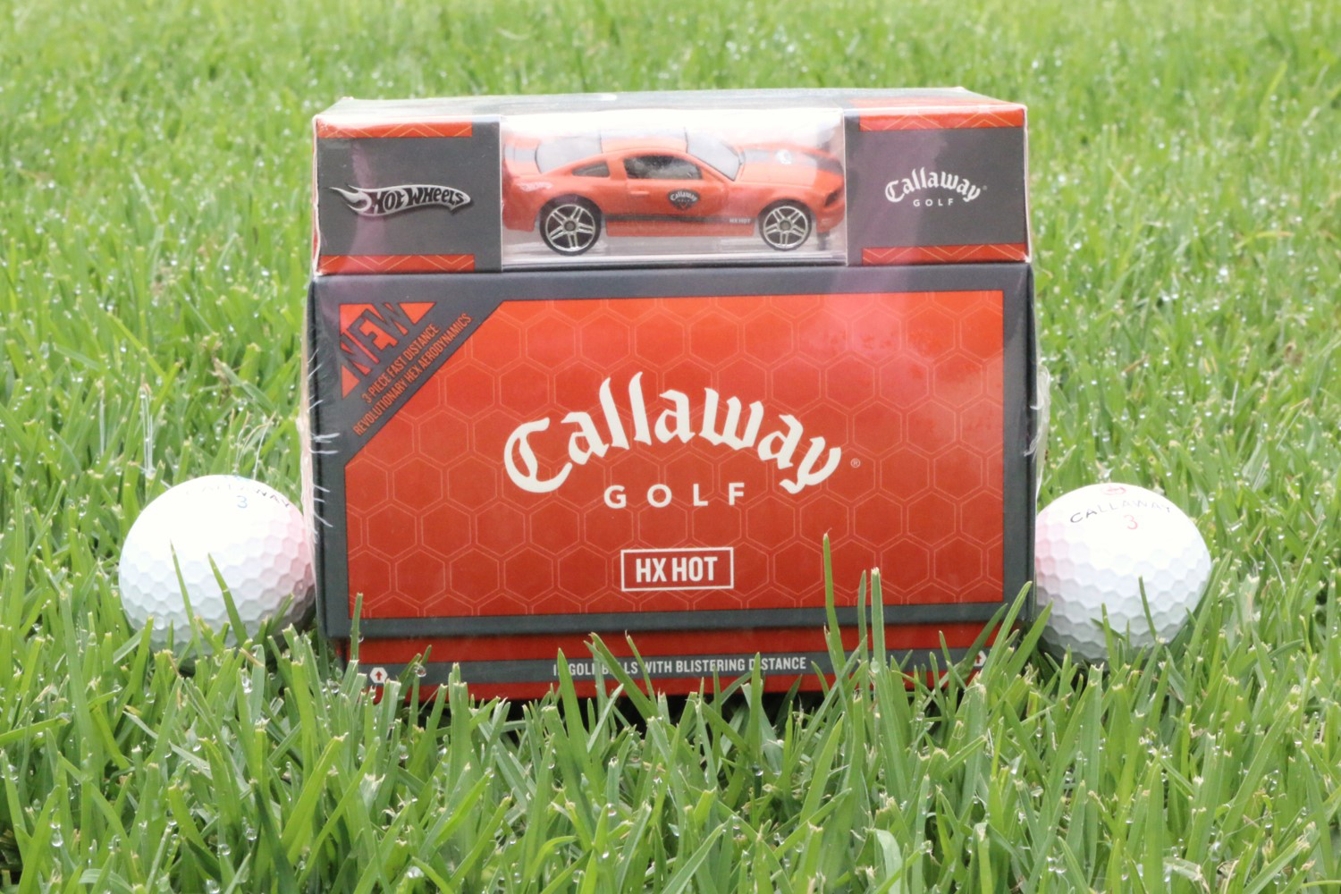 A red car is in the grass with golf balls.